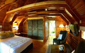 A cozy log cabin bedroom with a large bed, a chair, and a TV. - Senteur Vanille (Saint-Paul)
