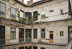 Un edificio de varios pisos con balcones, contraventanas verdes y plantas en macetas.
