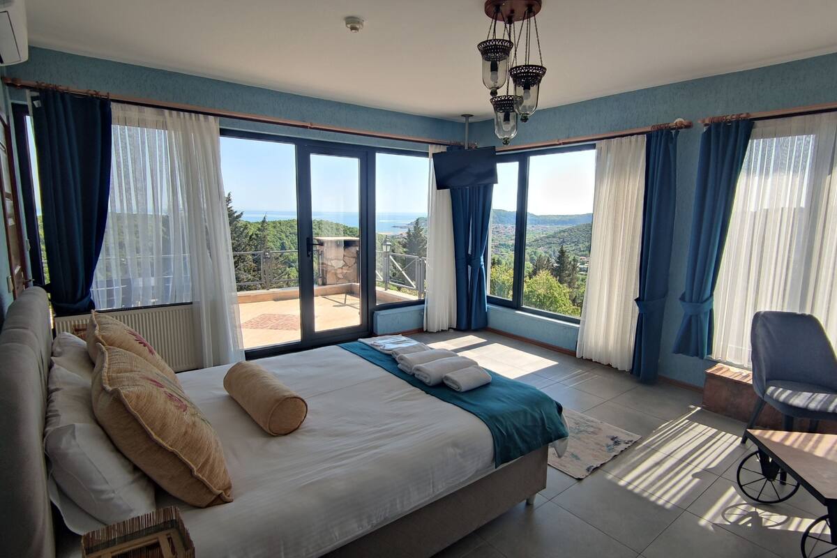 A bedroom with a large bed, a chair, and a view of the outdoors.
