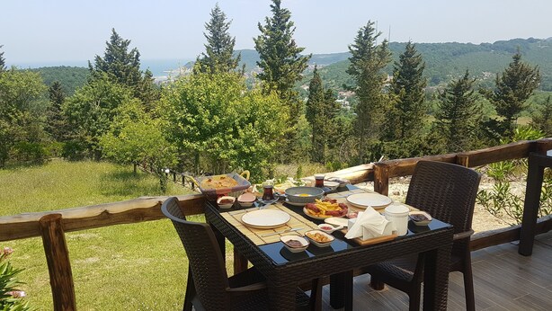 A table set outdoors with various dishes, surrounded by a wooden deck and overlooking a mountainous landscape. - Ağva Stone House Boutique (Sile)