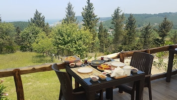 Mesa al aire libre con diversos platos, rodeada por una terraza de madera y con vistas a un paisaje montañoso.