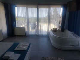 Una habitación con un gran ventanal corredero, una bañera de hidromasaje y una mesa de masajes con toallas.