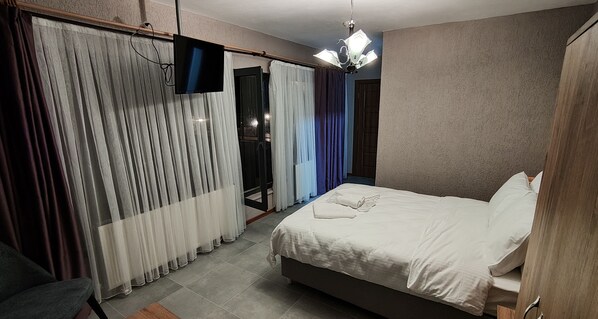 A bedroom with a bed, curtains, a television, and a chandelier.