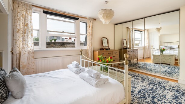 A hotel room with a bed, a dresser, a mirror, and a window with curtains. - Panoramic Family Home in Maida Vale (London)