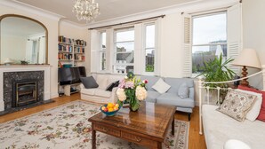 A living room with a fireplace, sofa, coffee table, and a bookshelf. - Panoramic Family Home in Maida Vale (London)