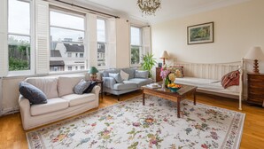 A living room with a sofa, a coffee table, a lamp, and a painting on the wall. - Panoramic Family Home in Maida Vale (London)