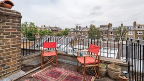 A balcony with two red chairs, a patterned rug, and potted plants. - Panoramic Family Home in Maida Vale (London)
