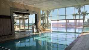 En indendørs swimmingpool med glasvægge, flisegulv og et skilt, der angiver poolens dybde.