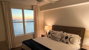Et hotelværelse med en stor seng, et sengebord med en lampe og havudsigt fra vinduet.