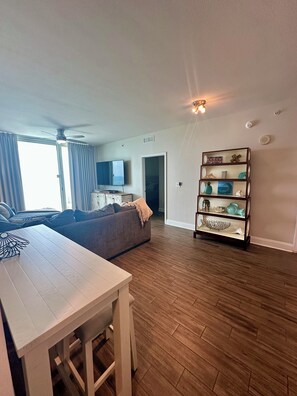 A modern living room with a wooden floor, a white table, a grey sofa, and a decorative shelf.