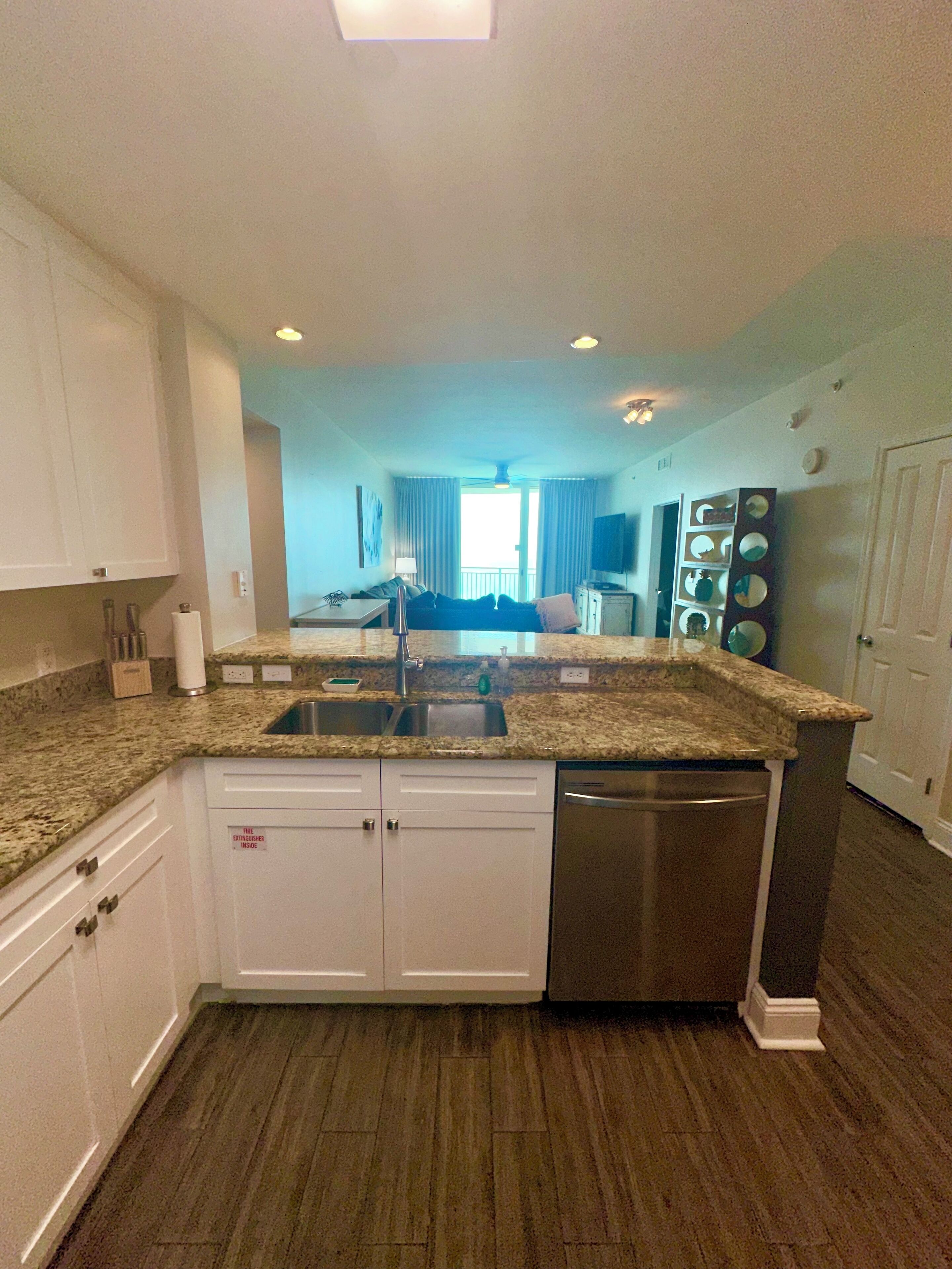 A modern kitchen with granite countertops, white cabinetry, a stainless steel dishwasher, and a built-in oven.