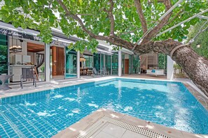 A swimming pool with a tree overhang, glass doors, and a modern interior design. - Hi At Home - 4BR Luxury Pool Villa in Pattaya (Pattaya)