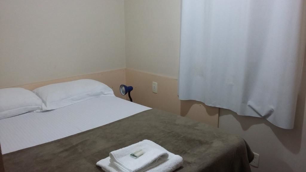 A hotel room with a bed, a bedside table with a lamp, and a curtain.