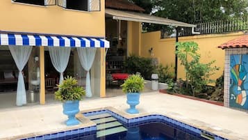 A pool area with a tiled edge, potted plants, and a building with a striped awning.