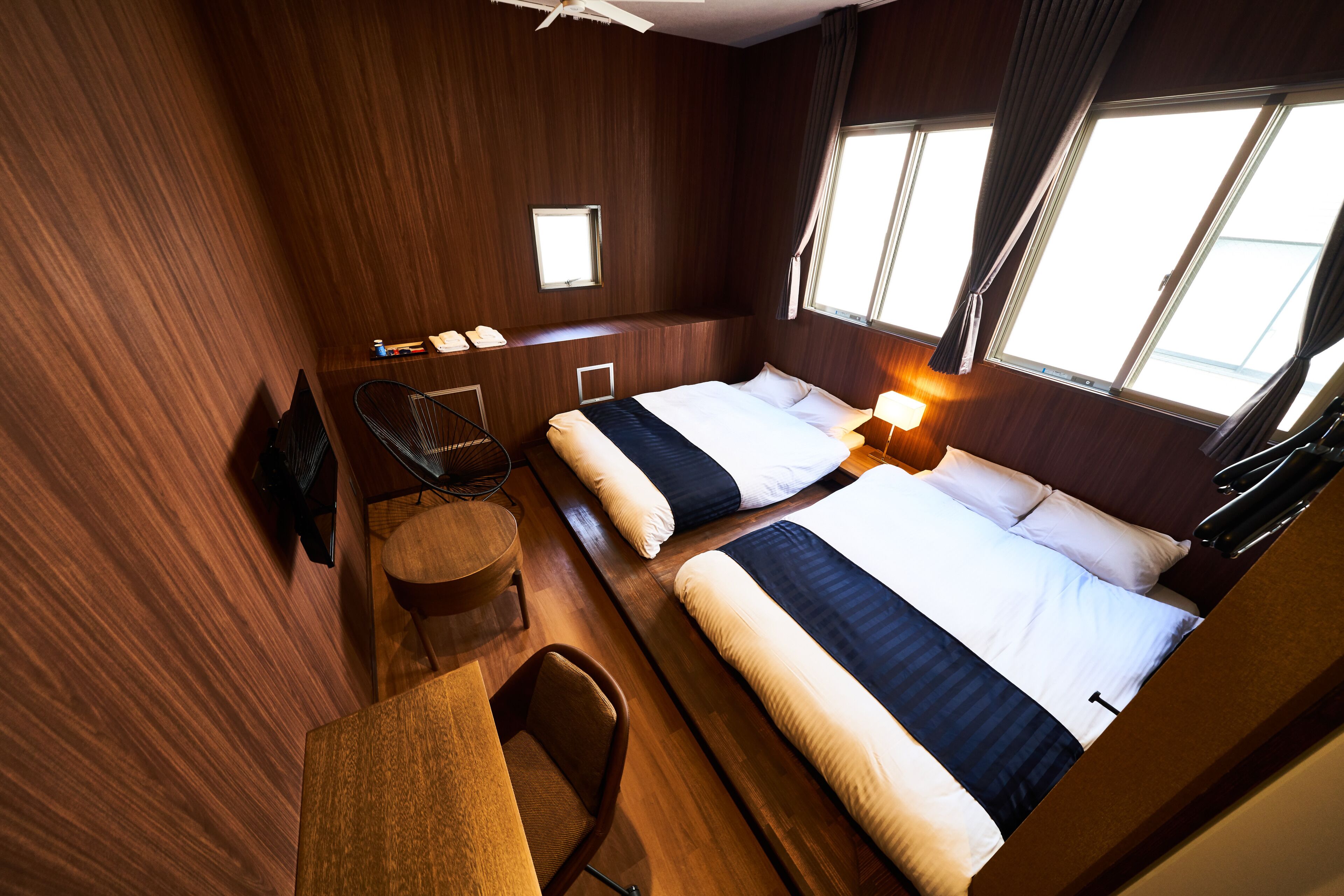 Ein Hotelzimmer mit zwei Betten, einem Schreibtisch, einem Stuhl, einem kleinen Tisch und einem Fenster mit Vorhängen.
