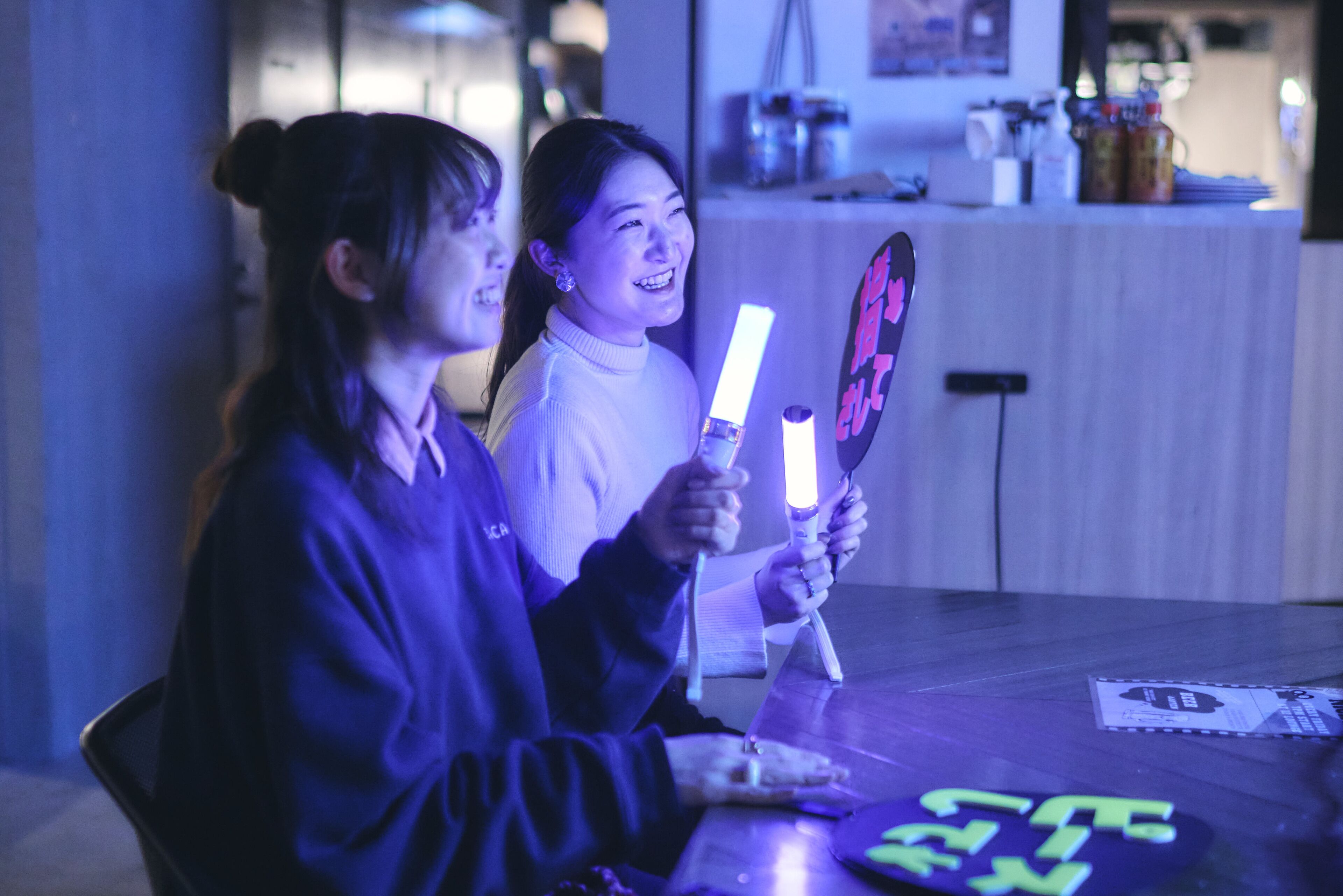 Two people holding glow sticks, sitting at a table with a menu and a coaster.
