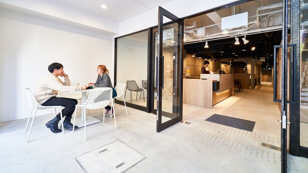 An office space with a glass partition separating a meeting area from a kitchen area.