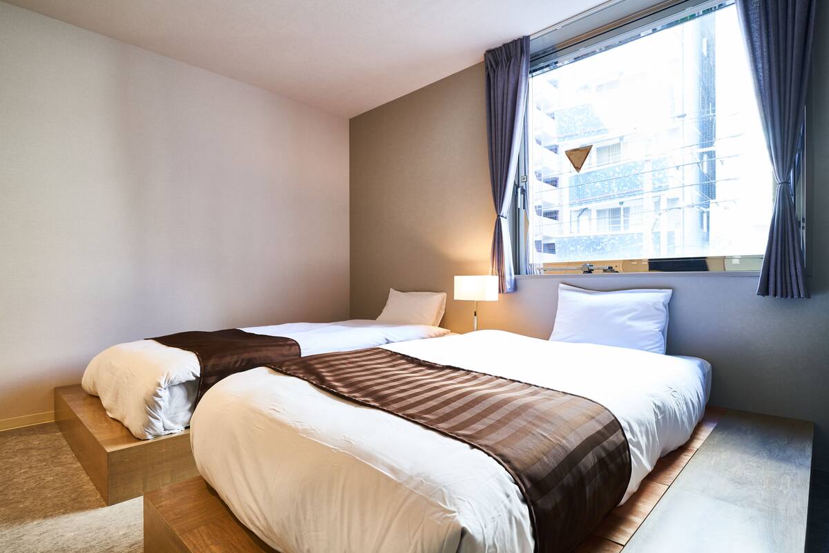 A hotel room with two beds, a window with curtains, and a lamp.