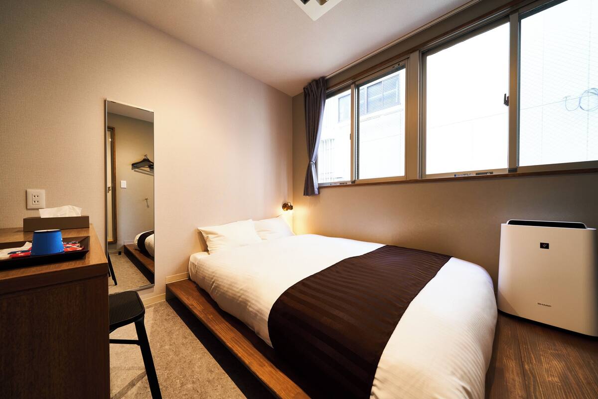 A hotel room with a bed, a desk, a chair, a wardrobe, and a window with curtains.