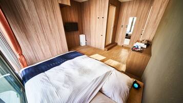 Una habitación de hotel moderna con una cama grande, paredes de madera, un televisor de pantalla plana, una mesita de noche pequeña y un baño con espejo y lavamanos.