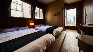 A hotel room with two beds, a desk, and a view of a building through the window.