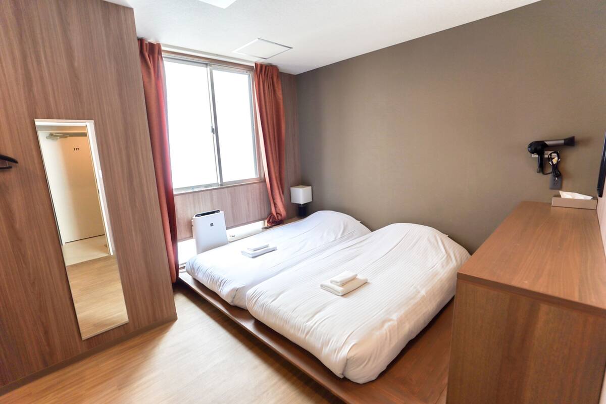 A hotel room with two beds, a desk, a lamp, and a window with curtains.