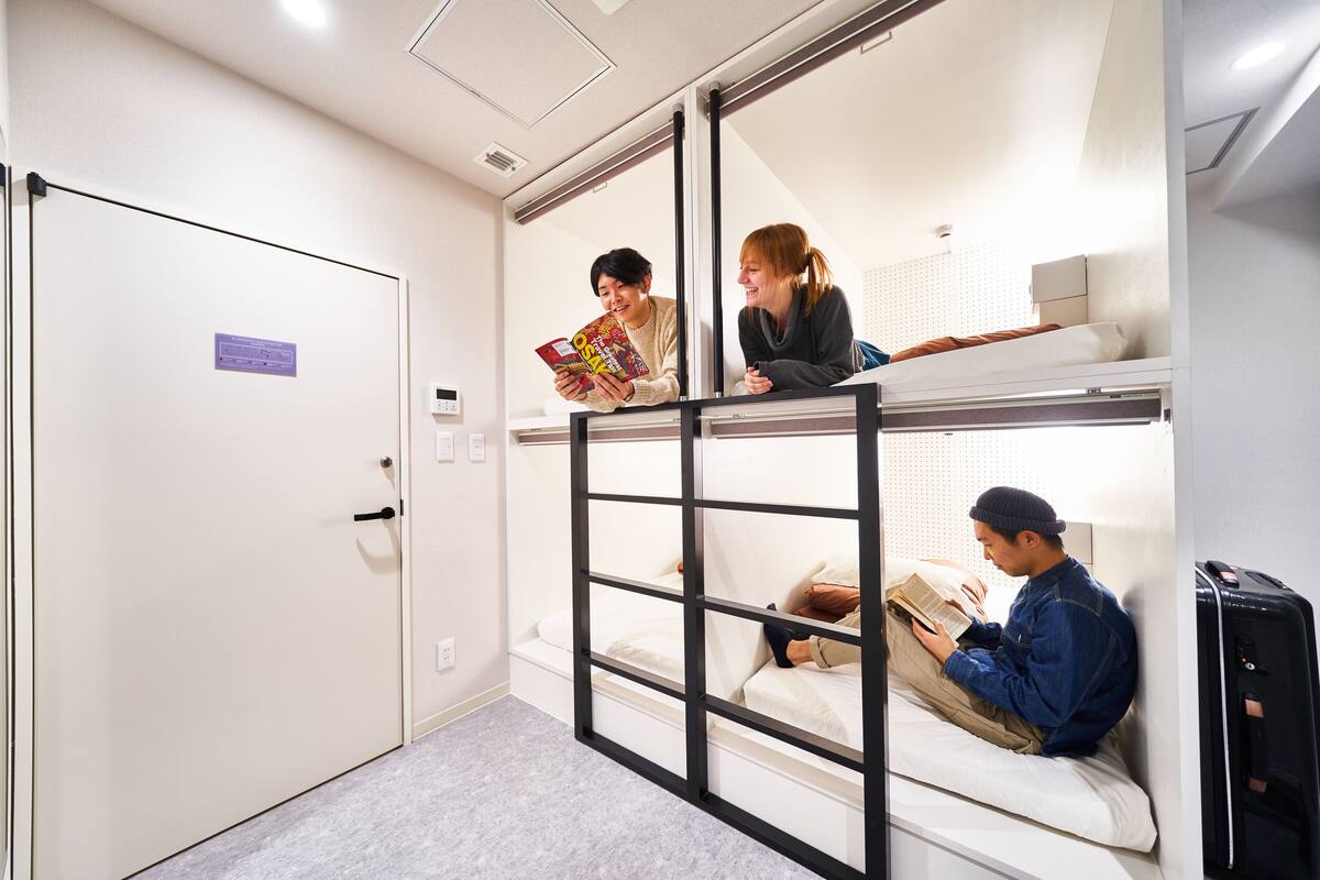 A dormitory room with bunk beds, a door, and a small desk with a computer.
