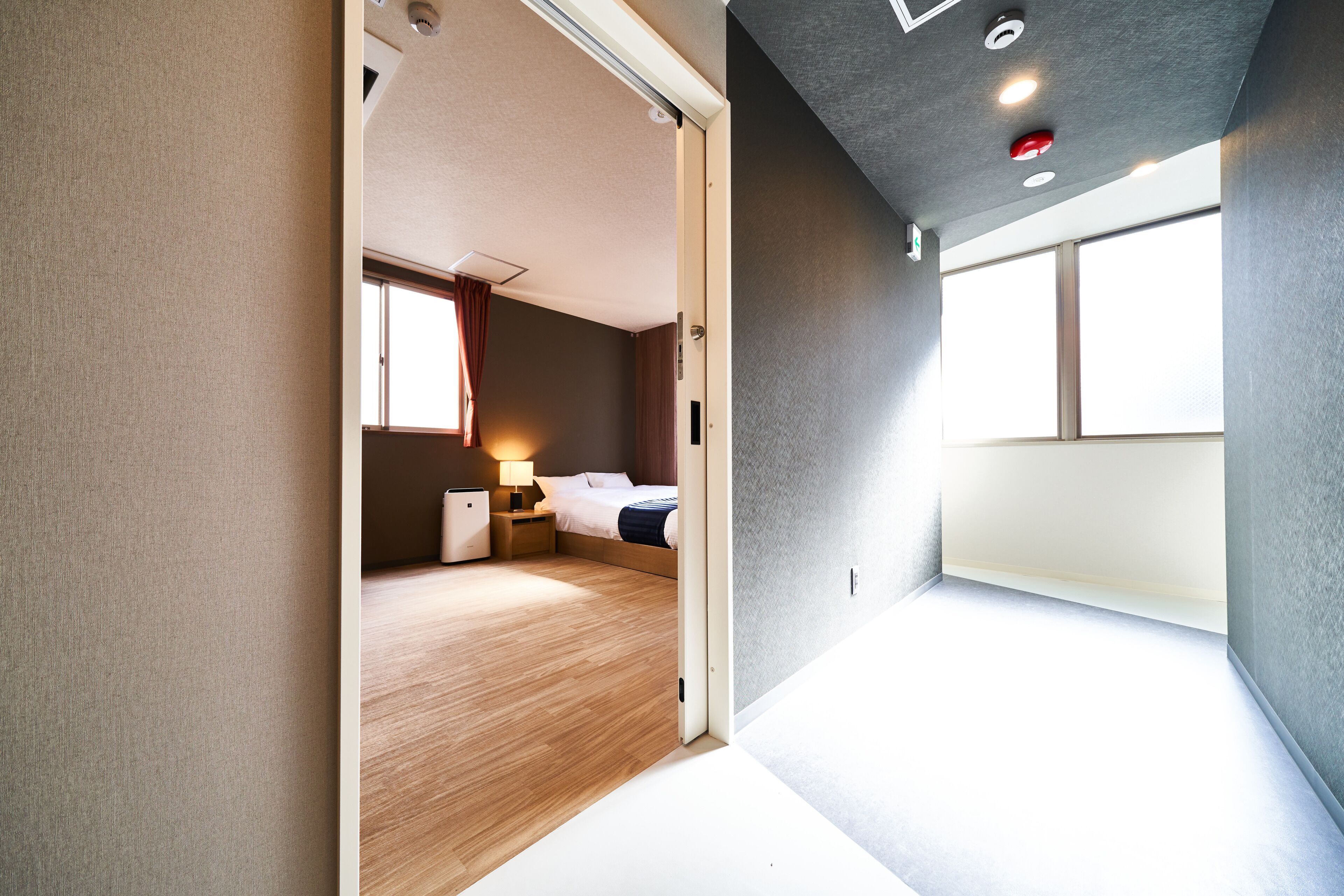 A modern hotel room with a bed, bedside table, lamp, and a view of the outside.