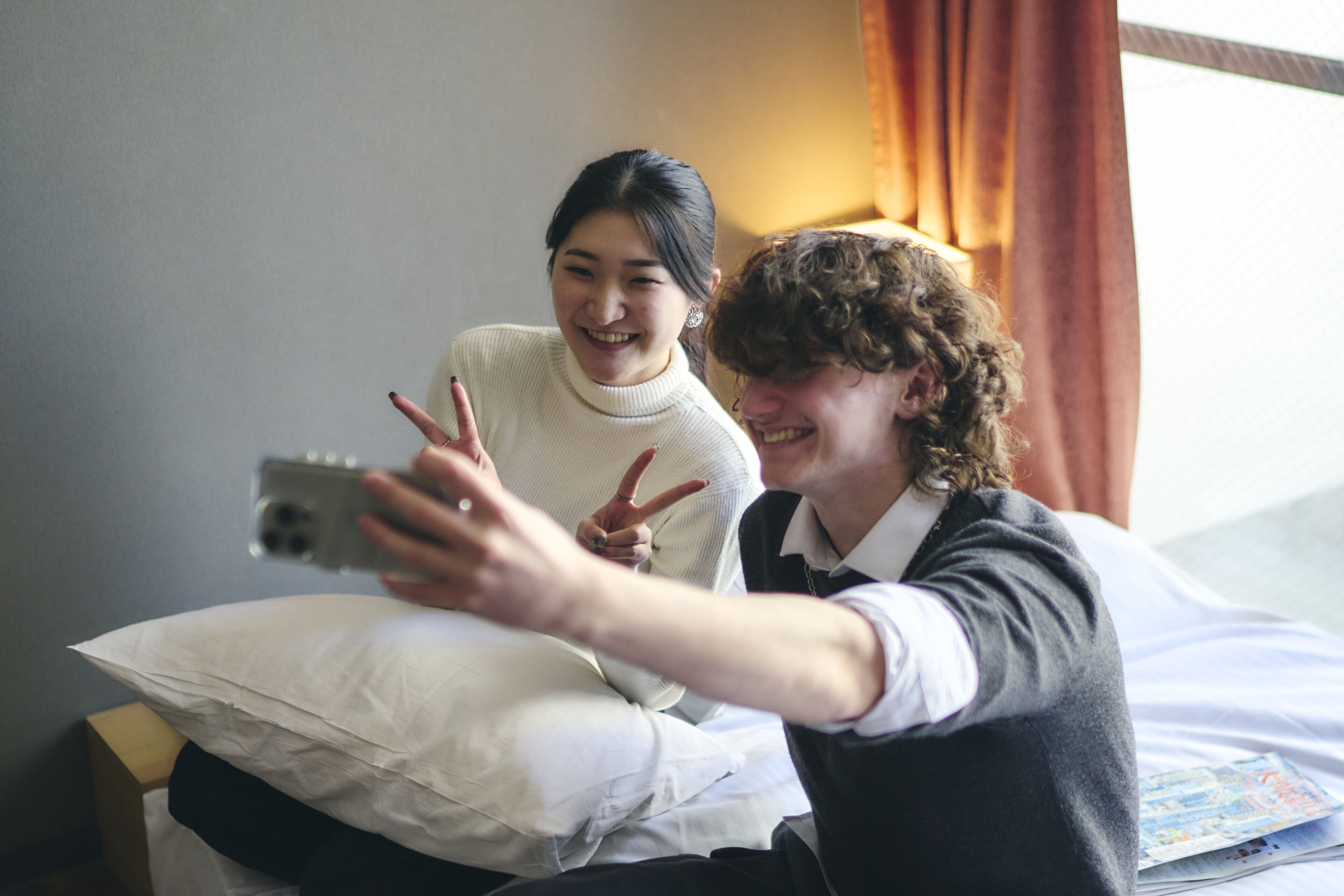 Two people sitting on a bed, one holding a smartphone.