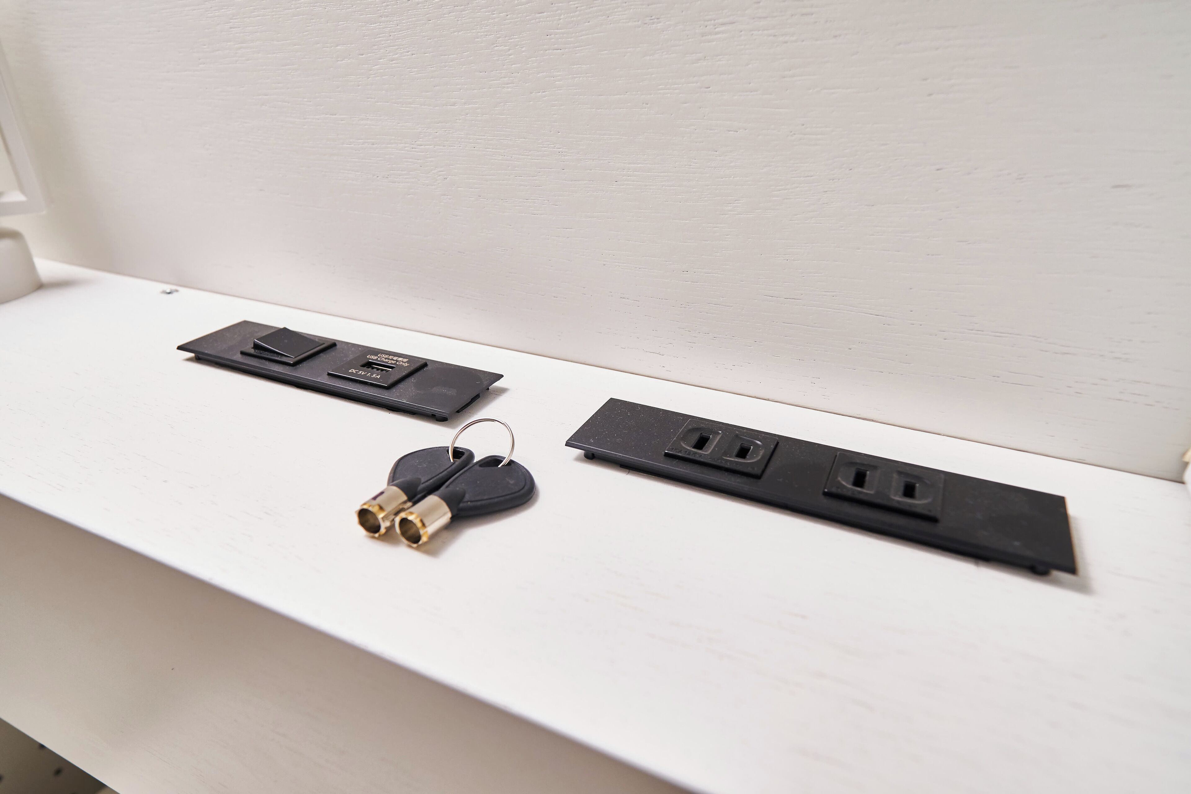 A white shelf with three black electrical adapters and a pair of keys.