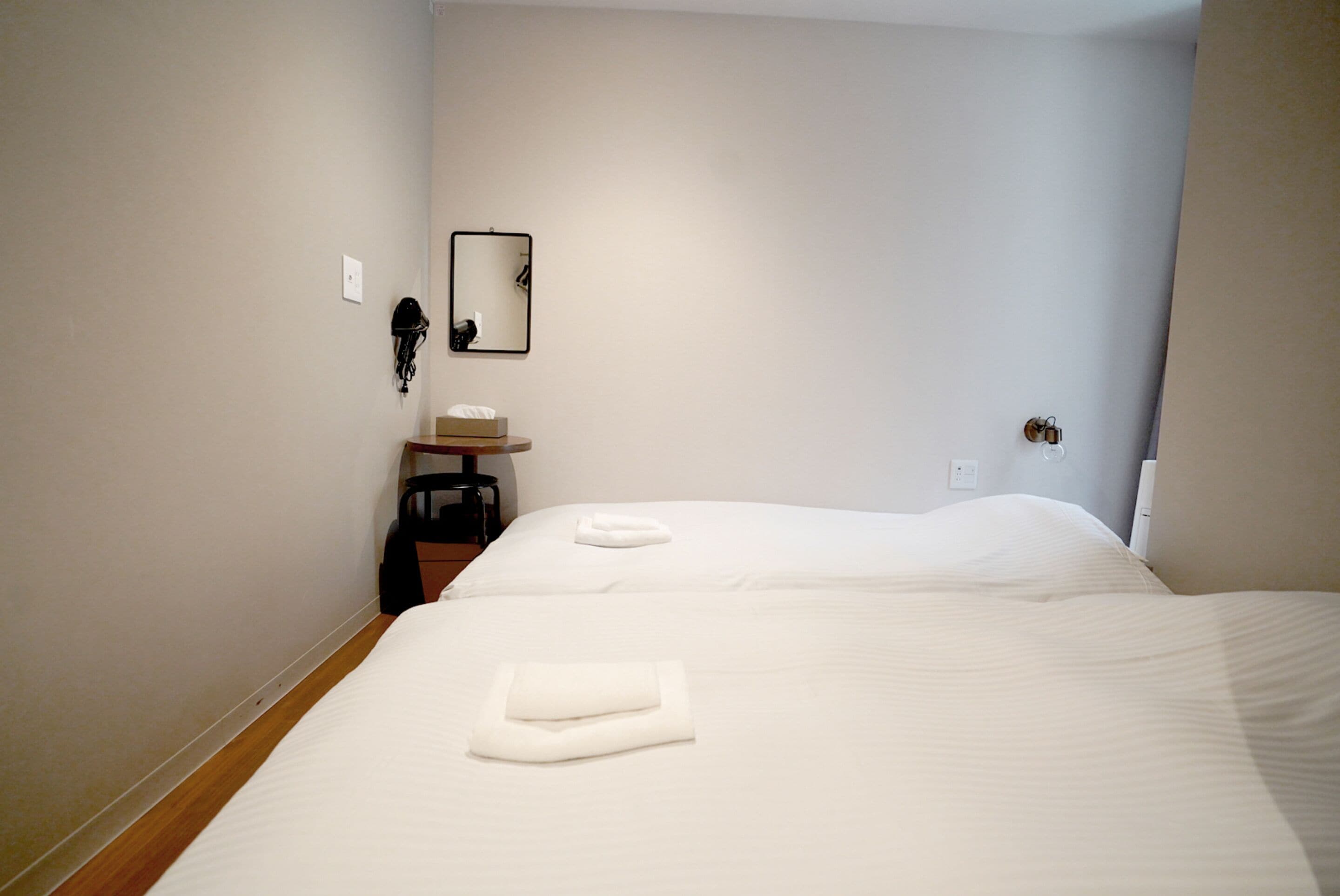 A hotel room with two beds, a small bedside table, a mirror, and a wall socket.