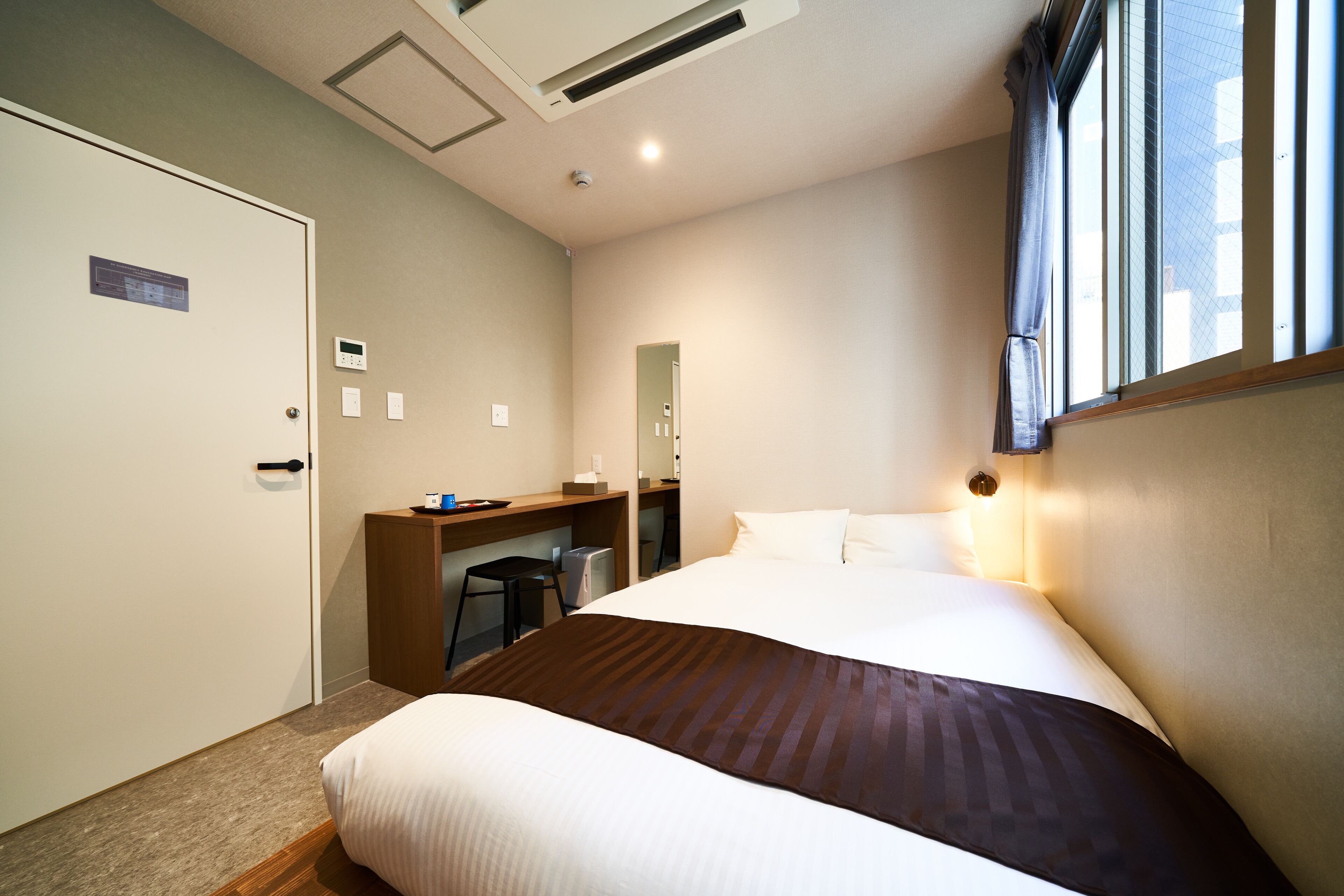 A hotel room with a bed, a desk, a chair, and a window.