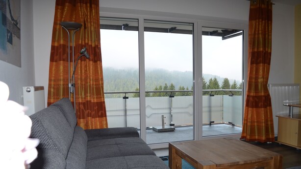 Un salón con un sofá gris, una mesa de centro de madera y vistas a un balcón con barandilla y árboles.