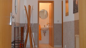 Un pasillo con puerta de madera, un espejo, un lavamanos y un esquirol.