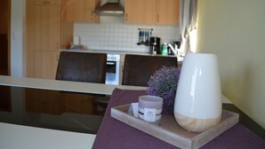 Ett kök med träskåp, vita kakelplattor ovanför arbetsbänken och ett fönster med gardiner.