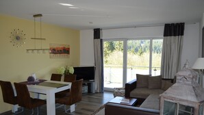 Ett vardagsrum med ett matbord, stolar, en soffa, en tv och ett stort fönster med gardiner.