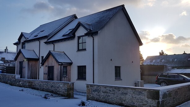 A two-story building with a stone wall in front, a wooden structure to the left, and a parked car to the right. - Linn of Avon Holiday Cottages (Ballindalloch)