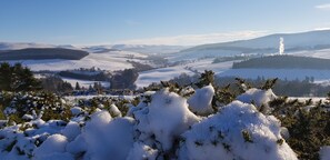 A snow-covered landscape with a distant view of a hill and a chimney emitting smoke. - Linn of Avon Holiday Cottages (Ballindalloch)