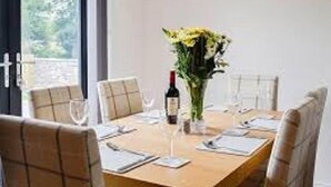 A dining table with chairs, a vase with flowers, wine glasses, and a bottle of wine. - Linn of Avon Holiday Cottages (Ballindalloch)