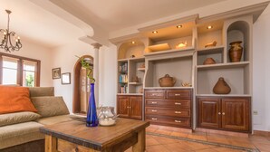 Una sala de estar acogedora con una mesa de centro de madera, un sofá con un cojín naranja y una estantería llena de libros y cerámica.