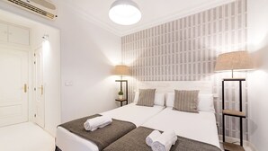 A hotel room with two beds, a large window with patterned curtains, a ceiling fan, and bedside lamps. - Genteel Home Chueca - Three Bedroom Apartment, Sleeps 5 (Madrid)