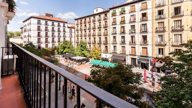 A balcony overlooking a courtyard with outdoor seating and a café, surrounded by multi-story buildings with balconies and windows. - Genteel Home Chueca - Three Bedroom Apartment, Sleeps 5 (Madrid)
