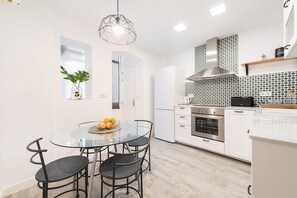 Een moderne keuken met een ronde glazen tafel, vier stoelen, een inbouwoven en een magnetron.