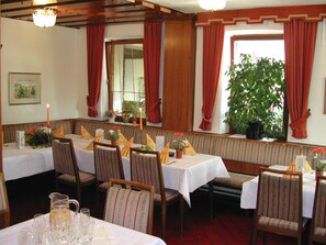 A restaurant with booths and tables, red curtains, and a large window with a view of greenery. - Fränkischer Gasthof Lutz (Giebelstadt)