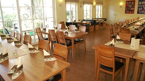 A spacious dining area with multiple wooden tables and chairs, large windows with curtains, and a view of greenery outside. - Fränkischer Gasthof Lutz (Giebelstadt)