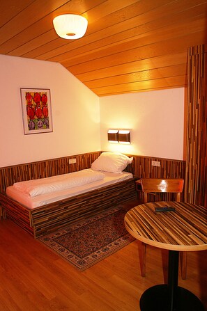 A compact room with a single bed, a small table, and a wall-mounted light fixture. - Fränkischer Gasthof Lutz (Giebelstadt)
