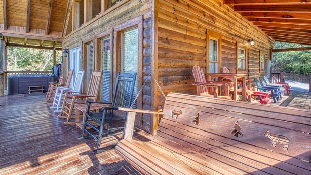 A log cabin with a covered porch, wooden chairs, and a table. - Game Room, Hot Tub, Wooded Views – Sleeps 12 – Near Dollywood & Pigeon Forge (Sevierville)