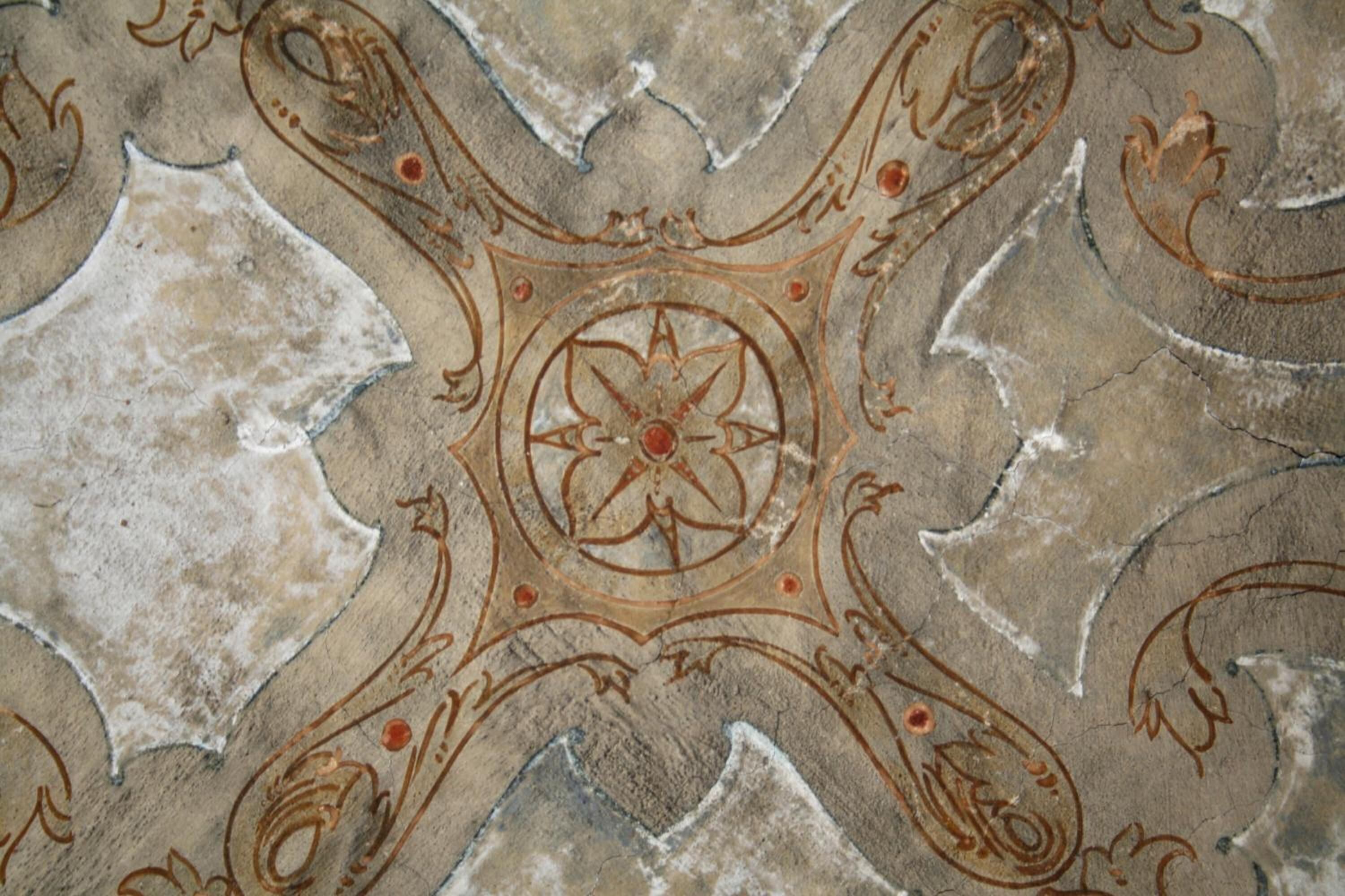 A ceiling with a geometric pattern featuring a central circular design surrounded by symmetrical shapes.