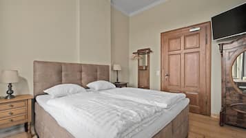 A bedroom with a large bed, wooden wardrobe, and a television.