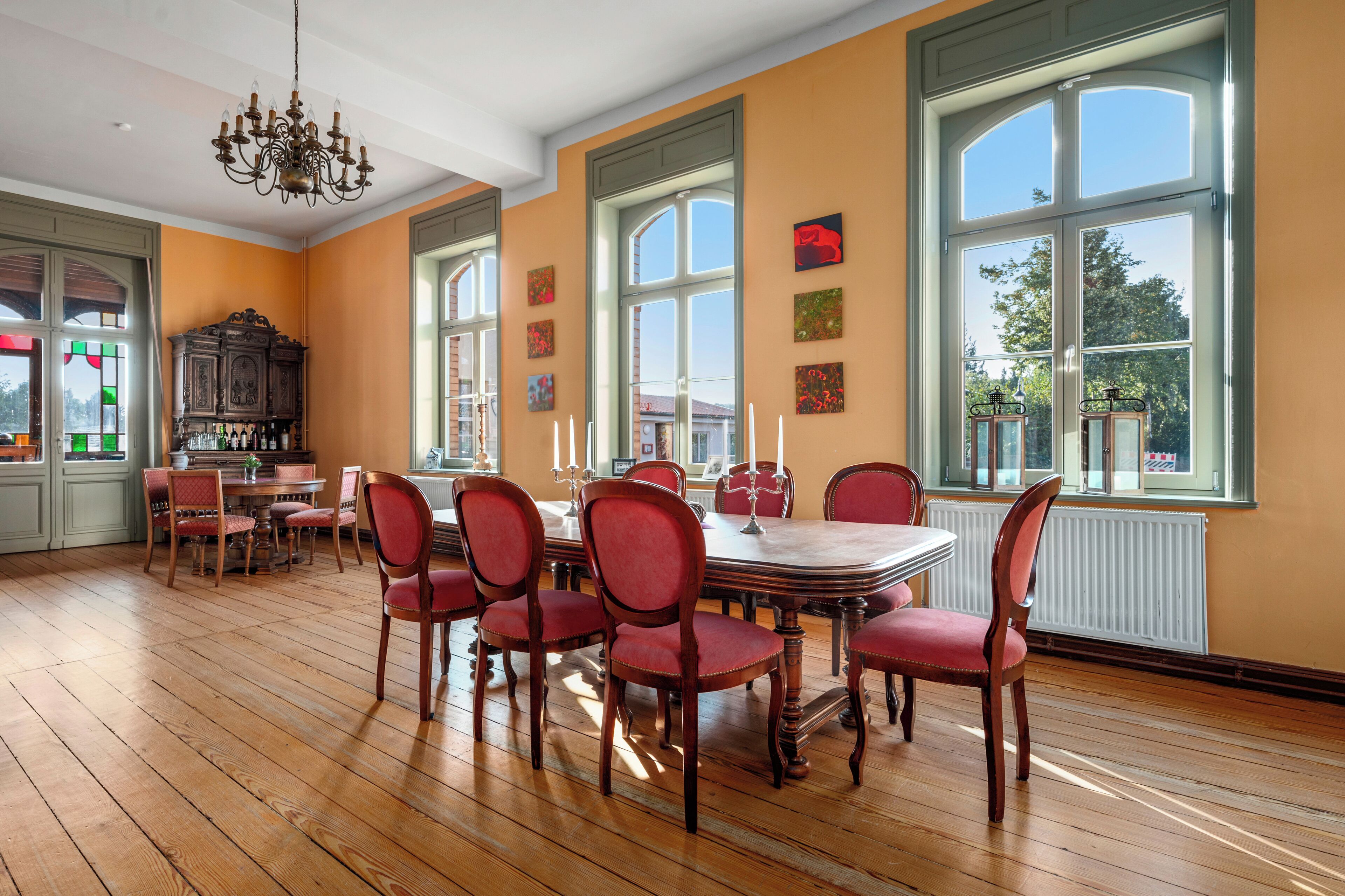 Un comedor con una mesa de madera y sillas rojas, ventanas amplias y una araña.